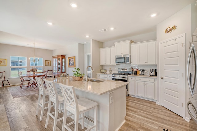 kitchen with appliances with stainless steel finishes, sink, light wood-type flooring, white cabinetry, and a kitchen island with sink