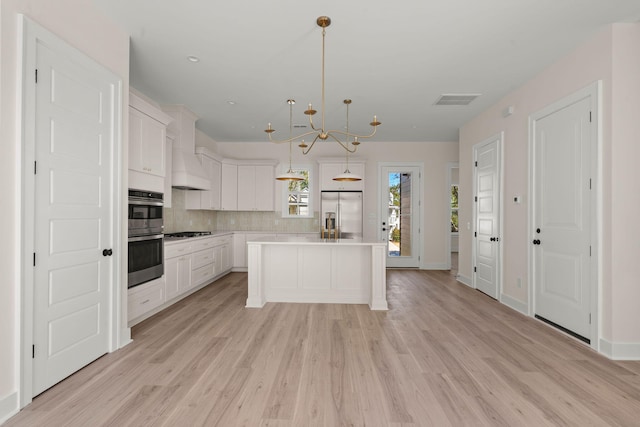 kitchen with white cabinets, appliances with stainless steel finishes, decorative light fixtures, a center island, and light countertops