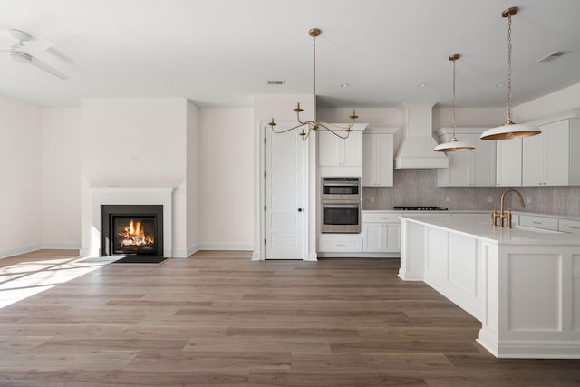 kitchen with white cabinets, custom range hood, hanging light fixtures, light countertops, and stainless steel double oven