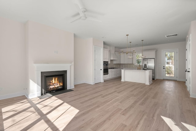 unfurnished living room featuring light wood finished floors, a fireplace with flush hearth, visible vents, and baseboards