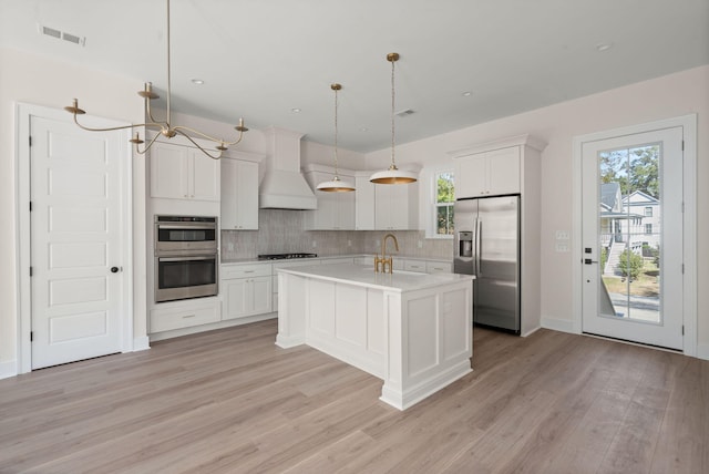 kitchen featuring premium range hood, light countertops, appliances with stainless steel finishes, an island with sink, and pendant lighting