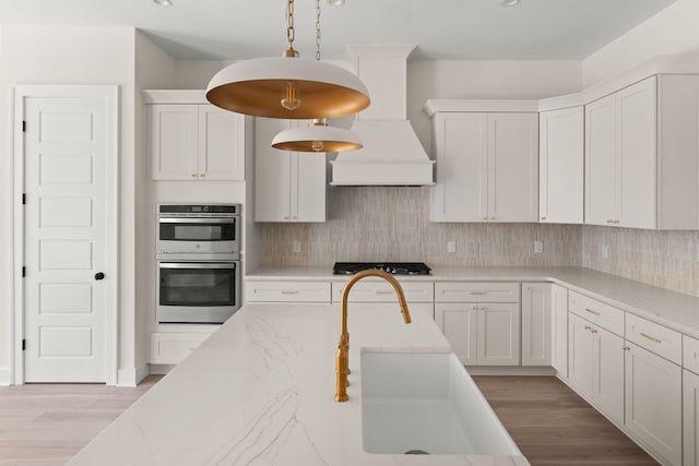 kitchen featuring light wood finished floors, decorative backsplash, hanging light fixtures, stainless steel appliances, and white cabinetry