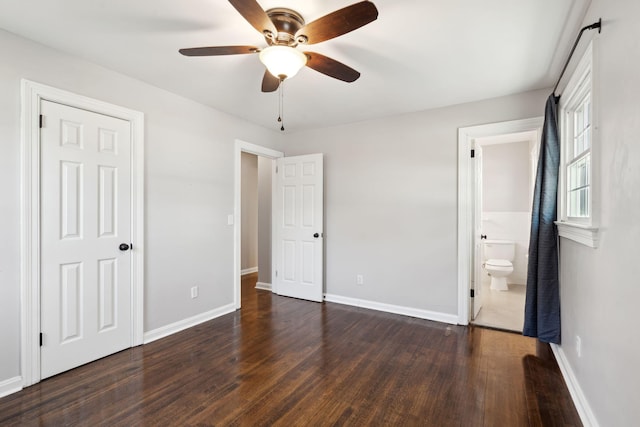 unfurnished bedroom with dark wood-style floors, ceiling fan, ensuite bath, and baseboards