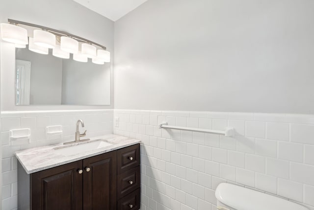 bathroom with a wainscoted wall, toilet, vanity, and tile walls