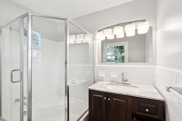 full bath with an enclosed shower, tile walls, vanity, and a wainscoted wall