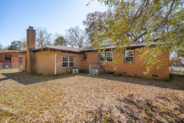 rear view of house with crawl space, a chimney, brick siding, and fence