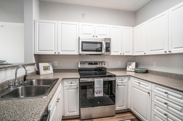 kitchen with white cabinets, sink, appliances with stainless steel finishes, and hardwood / wood-style floors