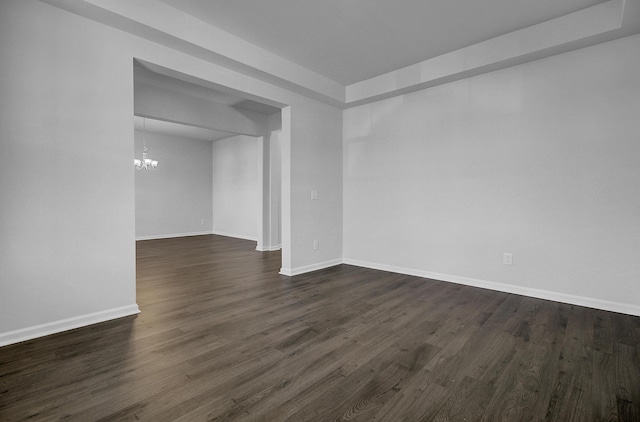 empty room featuring a chandelier, dark wood-type flooring, and baseboards