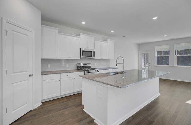 kitchen featuring stainless steel appliances, a sink, an island with sink, dark wood-style flooring, and backsplash