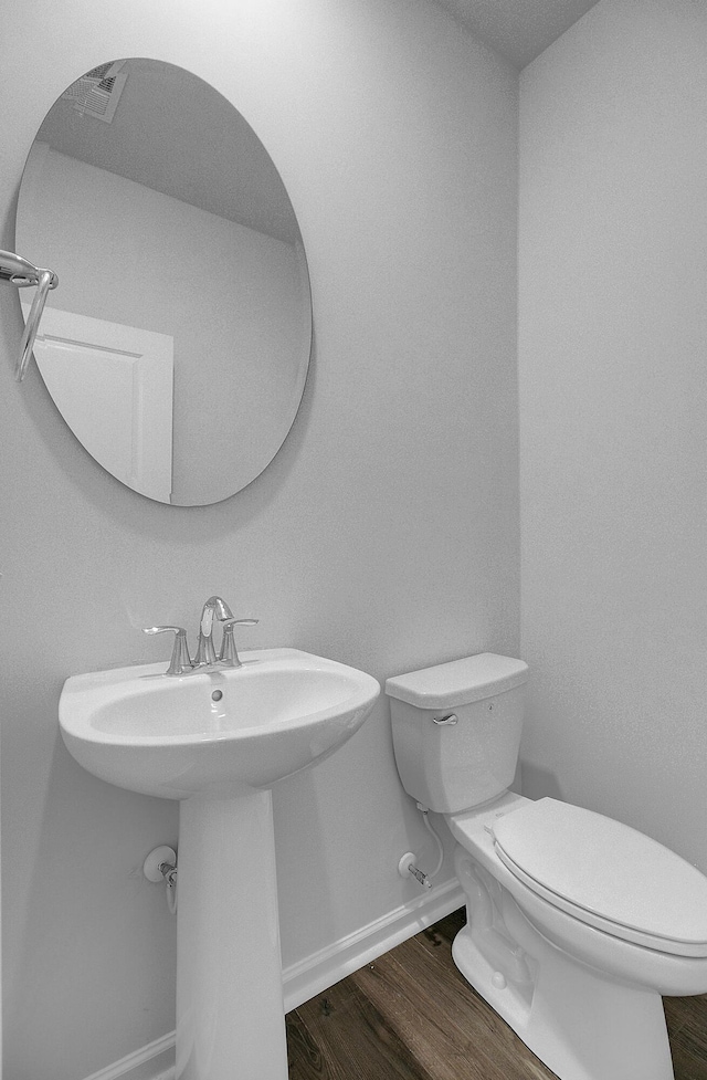 half bath with toilet, baseboards, wood finished floors, and a sink