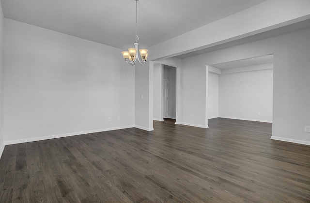 empty room featuring a chandelier, dark wood finished floors, and baseboards