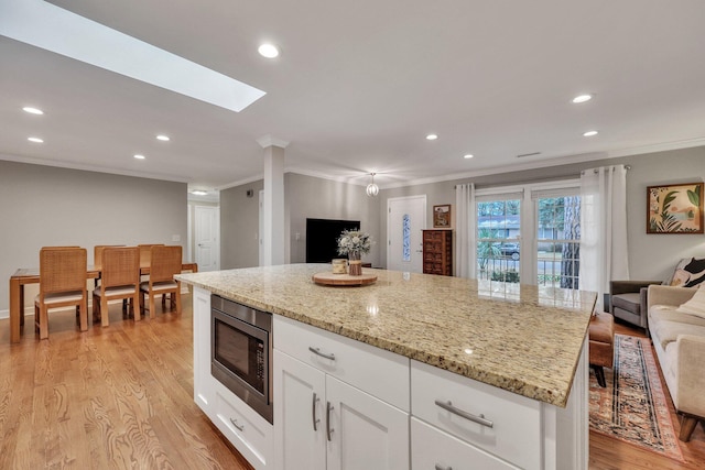 kitchen featuring crown molding, stainless steel microwave, light stone countertops, and white cabinets