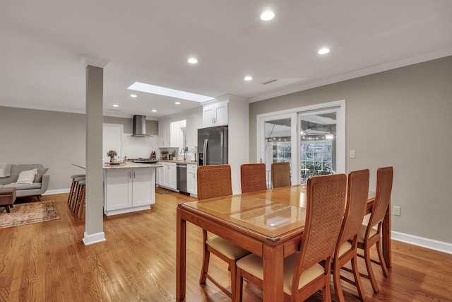 dining space featuring a skylight, ornamental molding, sink, and light hardwood / wood-style flooring