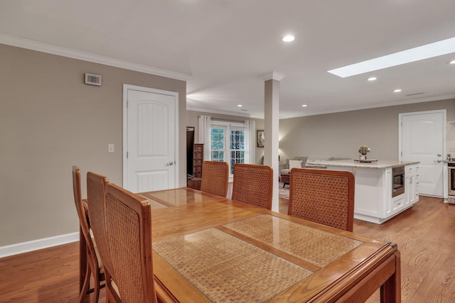 dining area with crown molding, a skylight, and light hardwood / wood-style floors