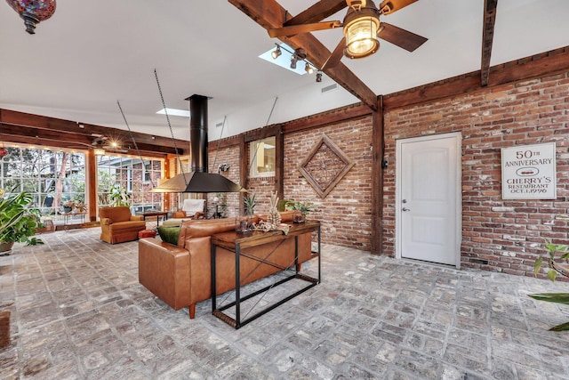 living room with beam ceiling, ceiling fan, and brick wall