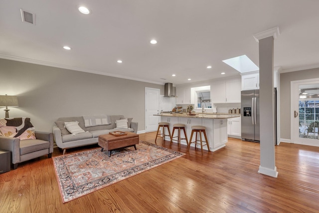 living room featuring ornamental molding, sink, a skylight, and light hardwood / wood-style floors