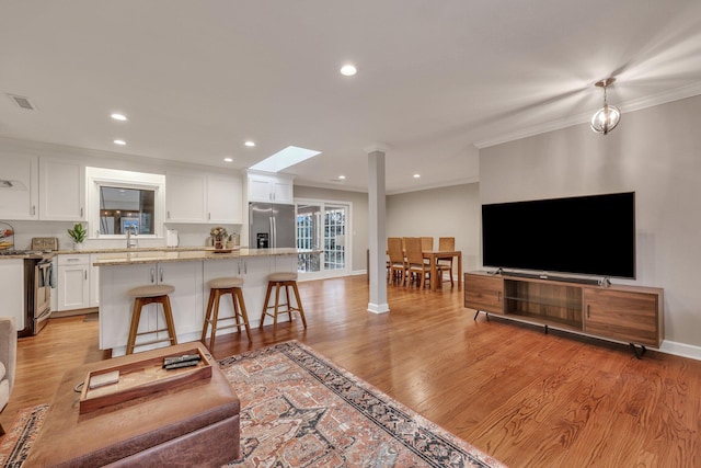 living room featuring ornamental molding, sink, a skylight, and light hardwood / wood-style floors