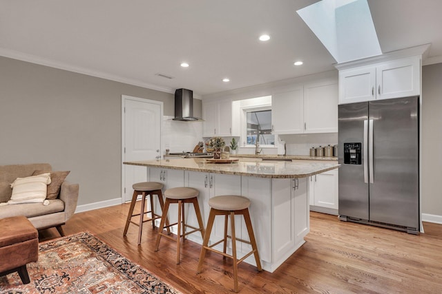 kitchen featuring stainless steel appliances, a kitchen island, wall chimney range hood, and white cabinets