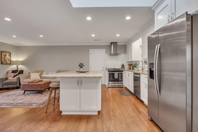 kitchen featuring white cabinetry, appliances with stainless steel finishes, a breakfast bar, and wall chimney range hood