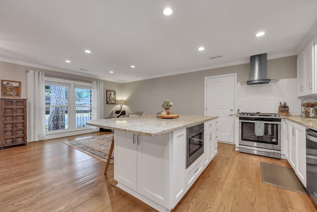 kitchen featuring white cabinetry, a kitchen breakfast bar, a center island, stainless steel appliances, and wall chimney range hood