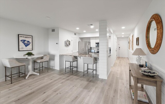 kitchen with kitchen peninsula, white cabinets, light hardwood / wood-style floors, and appliances with stainless steel finishes