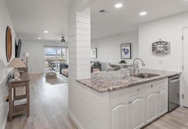 kitchen featuring dishwasher, sink, light stone counters, white cabinets, and light wood-type flooring