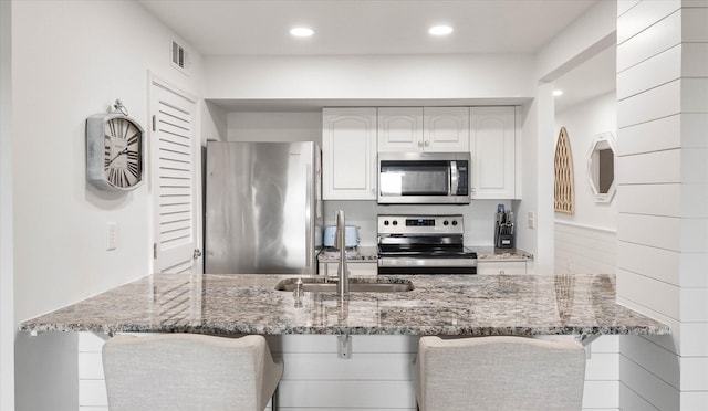 kitchen with a breakfast bar, dark stone countertops, white cabinetry, and stainless steel appliances