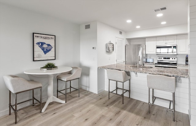 kitchen with appliances with stainless steel finishes, sink, light hardwood / wood-style floors, white cabinetry, and a breakfast bar area