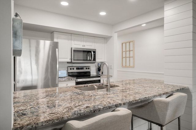 kitchen featuring a kitchen breakfast bar, light stone countertops, sink, and appliances with stainless steel finishes