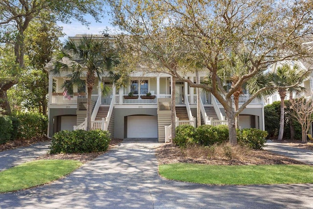 coastal home featuring aphalt driveway, an attached garage, a porch, and stairs