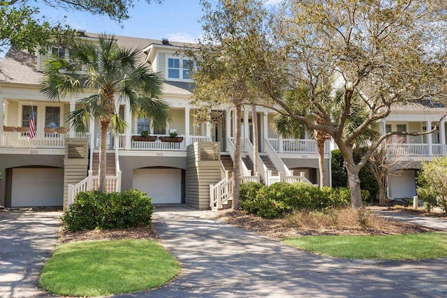 beach home featuring aphalt driveway, an attached garage, covered porch, and stairs