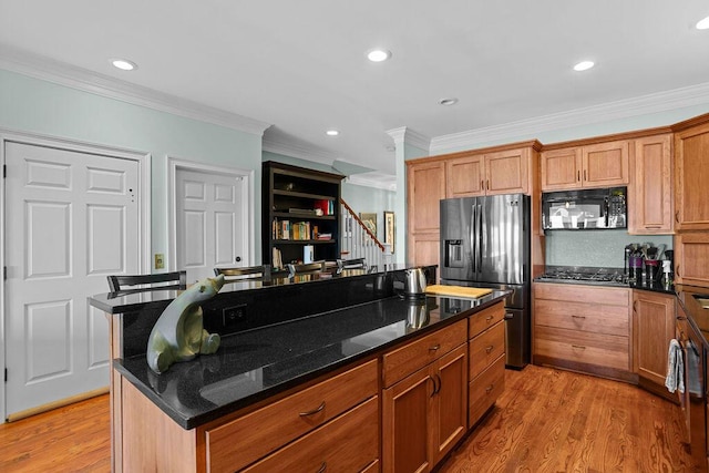 kitchen with light wood finished floors, crown molding, black microwave, dark stone counters, and fridge with ice dispenser