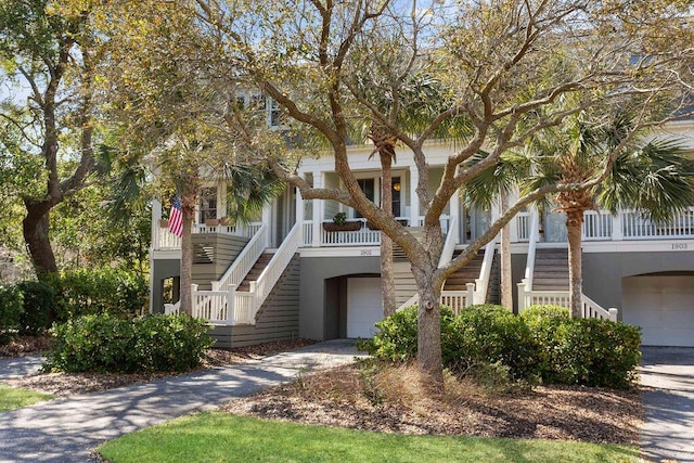 beach home with stairway, a garage, a porch, and concrete driveway