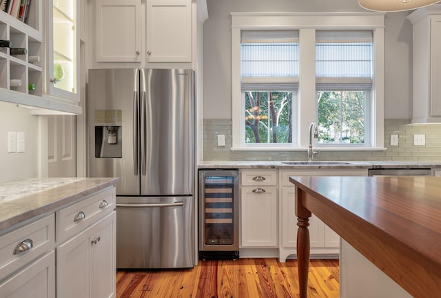 kitchen featuring stainless steel appliances, white cabinets, a sink, light wood-type flooring, and beverage cooler