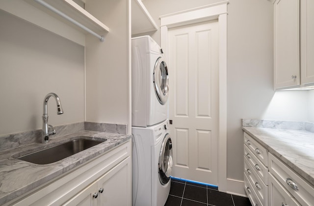 laundry area featuring stacked washer and dryer, dark tile patterned flooring, a sink, and cabinet space