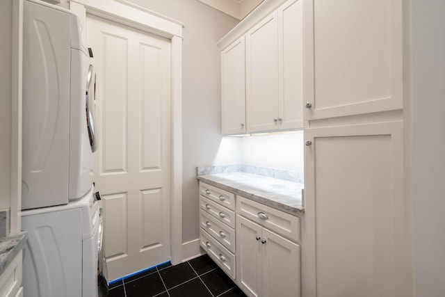 laundry area featuring dark tile patterned flooring, cabinet space, and stacked washer / drying machine