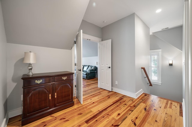 hallway featuring visible vents, light wood-style flooring, vaulted ceiling, an upstairs landing, and baseboards