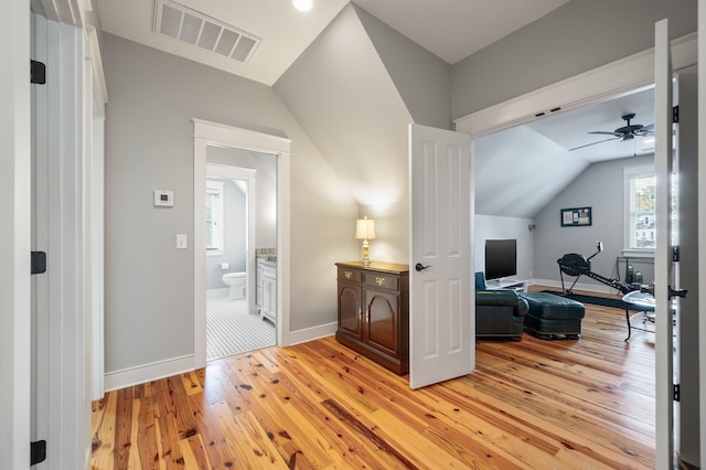 hallway featuring lofted ceiling, visible vents, light wood-style flooring, and baseboards