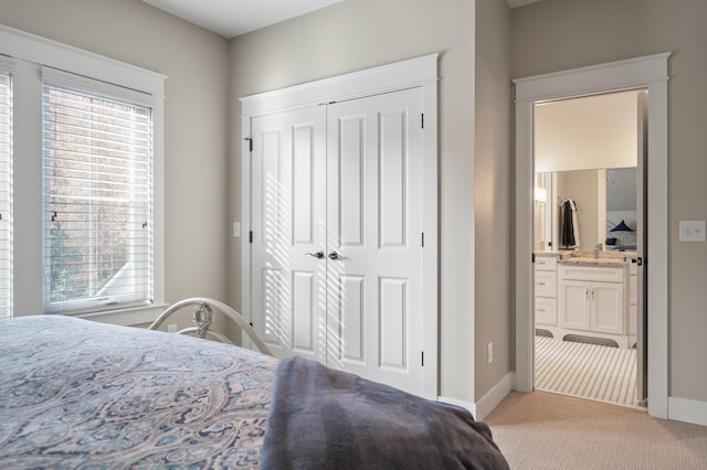 bedroom featuring a closet, light carpet, baseboards, and ensuite bathroom