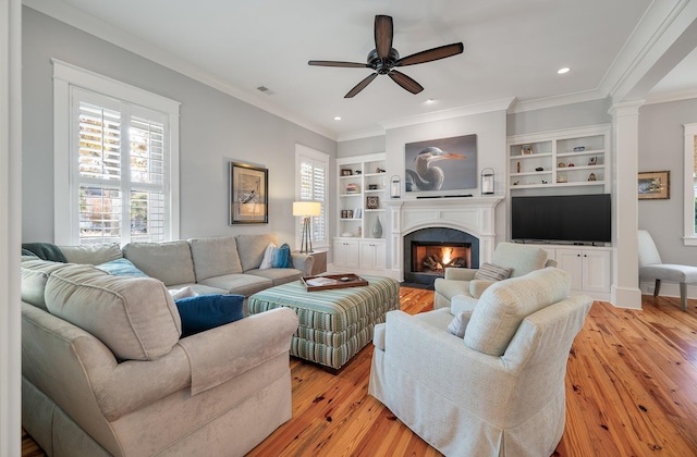 living area featuring built in features, visible vents, light wood-style floors, a fireplace with flush hearth, and ornate columns