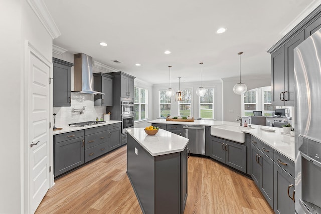 kitchen featuring crown molding, stainless steel appliances, gray cabinets, a sink, and wall chimney range hood