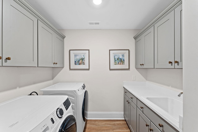 washroom featuring washer and clothes dryer, light wood finished floors, visible vents, cabinet space, and a sink