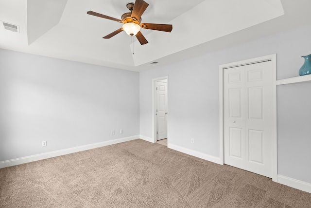 unfurnished bedroom featuring ceiling fan, a raised ceiling, a closet, and carpet