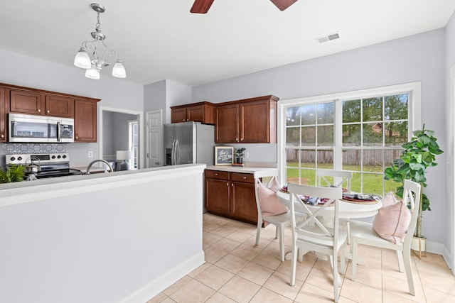 kitchen with pendant lighting, light tile patterned floors, backsplash, stainless steel appliances, and ceiling fan with notable chandelier