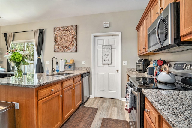 kitchen featuring appliances with stainless steel finishes, light wood-type flooring, sink, and light stone countertops