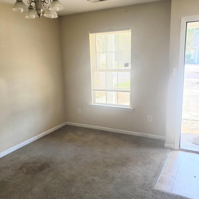 empty room with a chandelier, dark colored carpet, visible vents, and baseboards