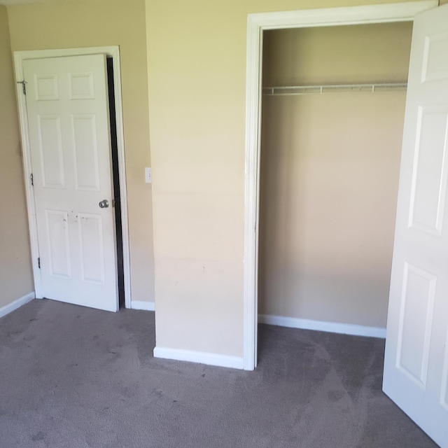 unfurnished bedroom featuring a closet, dark carpet, and baseboards