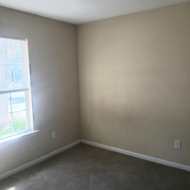 empty room featuring dark colored carpet and baseboards