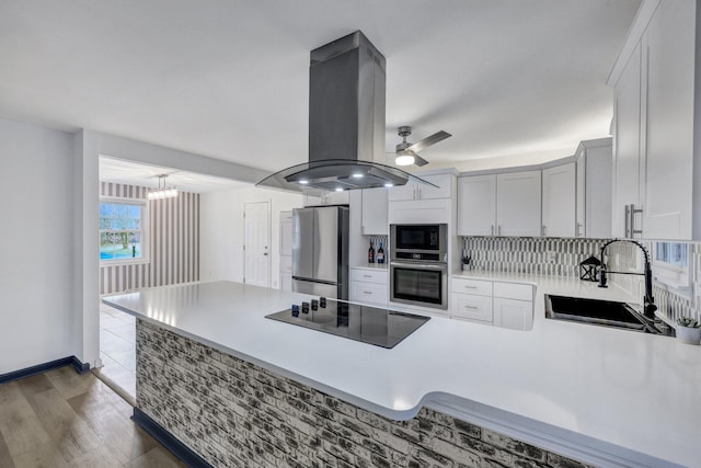 kitchen with light countertops, a peninsula, island exhaust hood, black appliances, and a sink