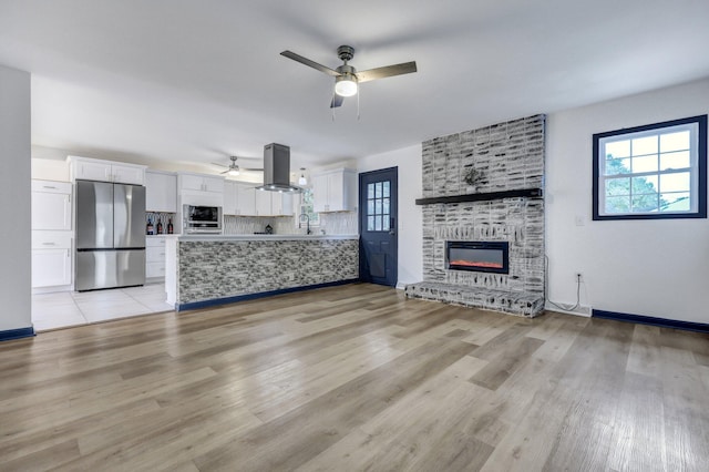 unfurnished living room featuring a ceiling fan, a sink, a fireplace, light wood finished floors, and baseboards